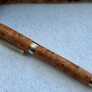 Puede incluir: Pluma de madera artesanal con clip y detalles dorados. El cuerpo de la pluma presenta un patr&oacute;n de veta de madera natural de color marr&oacute;n claro. Instrumento de escritura.