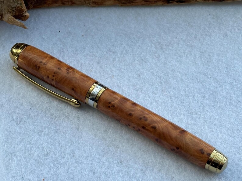 Puede incluir: Pluma de madera artesanal con clip y detalles dorados. El cuerpo de la pluma presenta un patr&oacute;n de veta de madera natural de color marr&oacute;n claro. Instrumento de escritura.