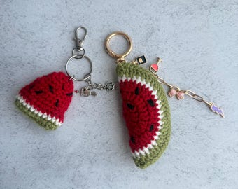 May include: Two crochet watermelon slice keychains. The smaller one has a silver ring with a heart and crown charm. The larger one has a gold ring with a chain featuring a perfume bottle, wine glass, bow, and purple lightning bolt charm.