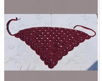 May include: A deep burgundy triangular crochet bandana featuring an intricate openwork shell stitch pattern throughout the body. The edges are finished with a scalloped border, and two thin crocheted ties extend from the top corners for fastening.