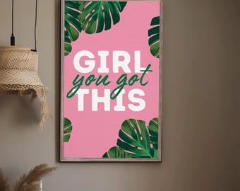 May include: A framed pink art print with the words "GIRL you got THIS" in white and green lettering. The print is decorated with green monstera leaves. The artwork is displayed on a grey wall.