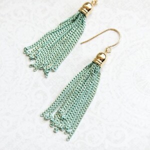 May include: A pair of long, mint green tassel earrings with gold hooks and a gold bead at the top of each tassel.