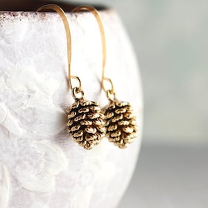 May include: Gold tone dangle earrings featuring a detailed pine cone design.