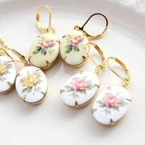 May include: Four pairs of gold tone earrings with oval shaped porcelain charms featuring floral designs. The charms have a white background with pink, yellow, and green floral patterns.