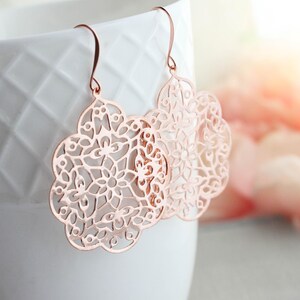 May include: Rose gold earrings featuring a delicate, intricate floral design. The earrings are lightweight and dangle from a simple hook.