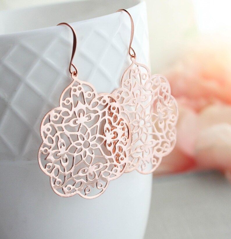 May include: Rose gold earrings featuring a delicate, intricate floral design. The earrings are lightweight and dangle from a simple hook.