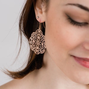 May include: Rose gold filigree earrings with a delicate, intricate design. The earrings are dangle style and feature a circular shape.