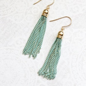 May include: A pair of long, mint green tassel earrings with gold-toned hooks and tops. The tassels are made of thin, linked chains.