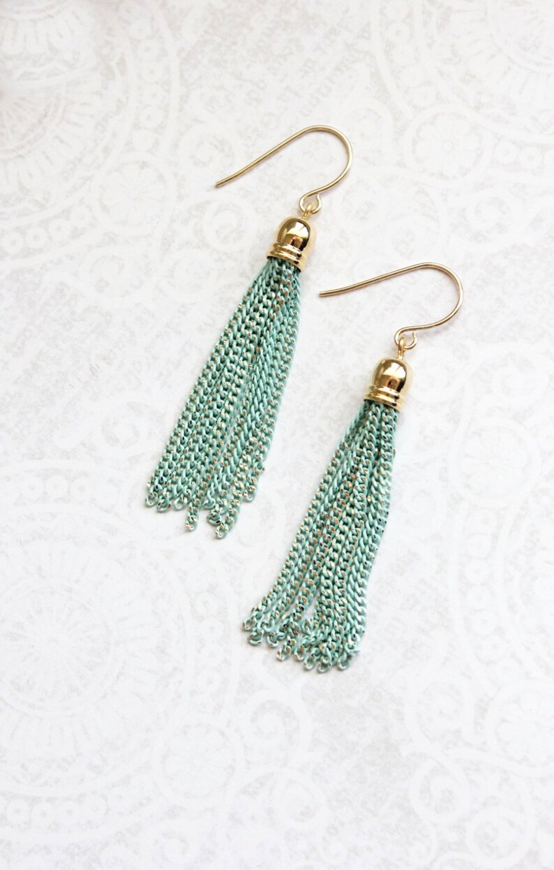 May include: A pair of long, mint green tassel earrings with gold-toned hooks and tops. The tassels are made of thin, linked chains.