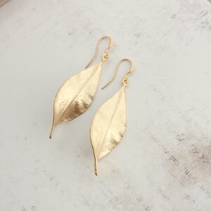 K&ouml;nnte beinhalten: Ein Paar goldene Ohrringe in Blattform. Die Ohrringe sind aus strukturiertem Metall gefertigt und haben ein schlichtes, elegantes Design.