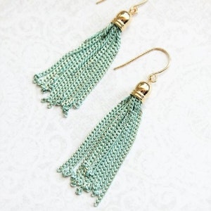 May include: A pair of mint green tassel earrings with gold hooks and tops. The tassels are made of chain links.