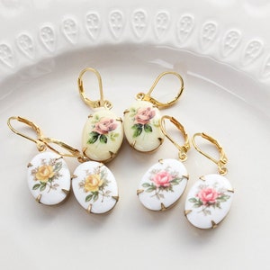 May include: Four pairs of gold tone earrings with oval shaped porcelain charms featuring floral designs. The charms have a white background with pink, yellow, and green floral patterns.