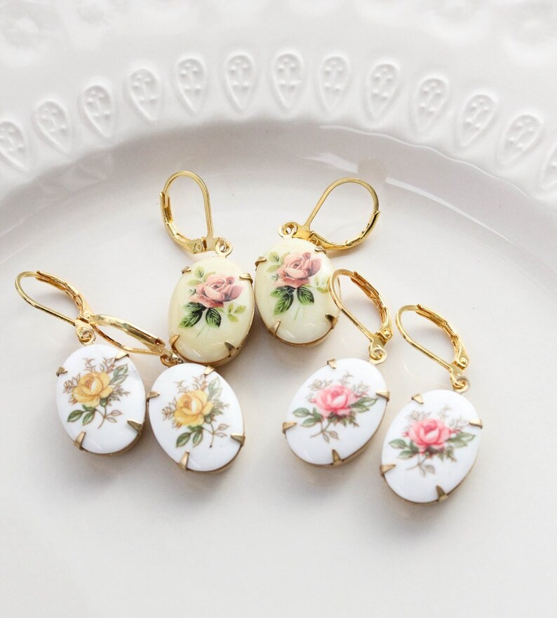 May include: Four pairs of gold tone earrings with oval shaped porcelain charms featuring floral designs. The charms have a white background with pink, yellow, and green floral patterns.