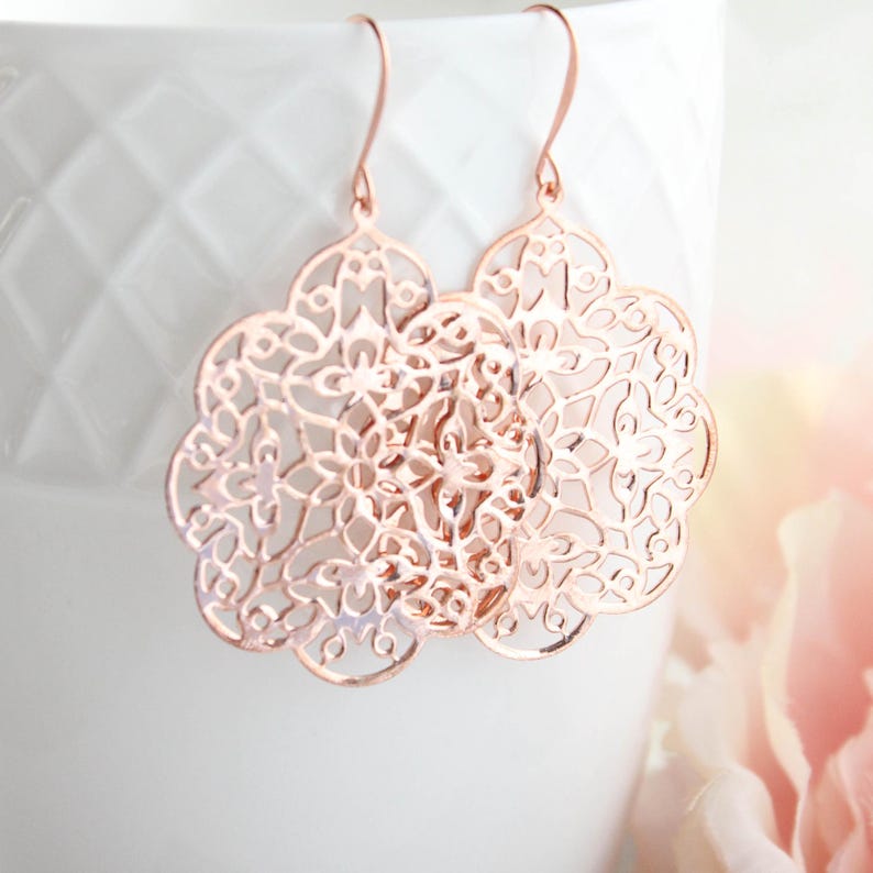May include: Rose gold filigree earrings with a delicate floral design. The earrings are lightweight and dangle from a hook.