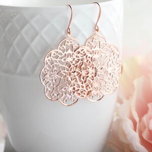 May include: Rose gold filigree earrings with a delicate floral design. The earrings are lightweight and dangle from a simple hook.