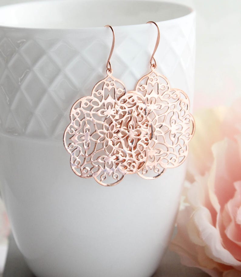 May include: Rose gold filigree earrings with a delicate floral design. The earrings are lightweight and dangle from a simple hook.