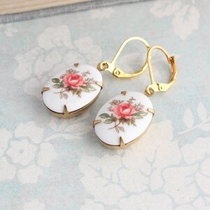 May include: A pair of gold tone earrings with white porcelain oval shaped charms featuring a pink rose floral design.