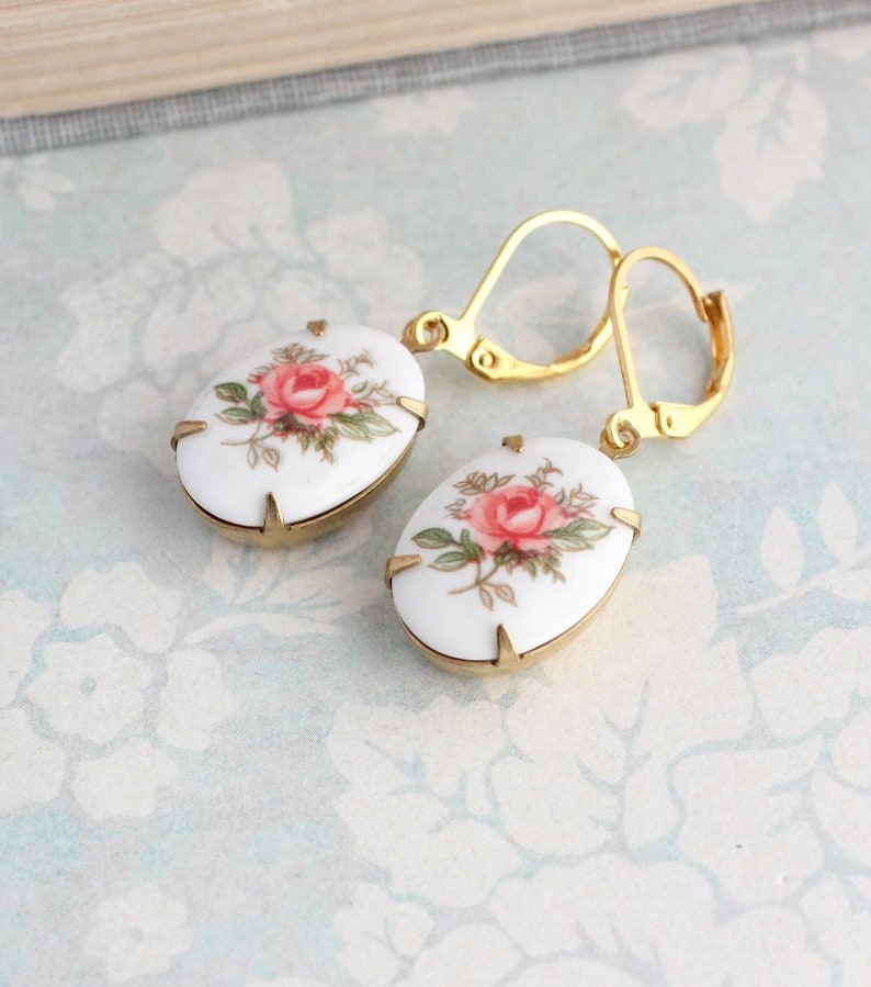 May include: A pair of gold tone earrings with white porcelain oval shaped charms featuring a pink rose floral design.