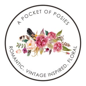 May include: A circular logo with the text "A Pocket of Posies" in a black circle. The text "Romantic. Vintage Inspired. Floral" is written around the circle. The logo features a watercolour illustration of a bouquet of pink and white flowers.