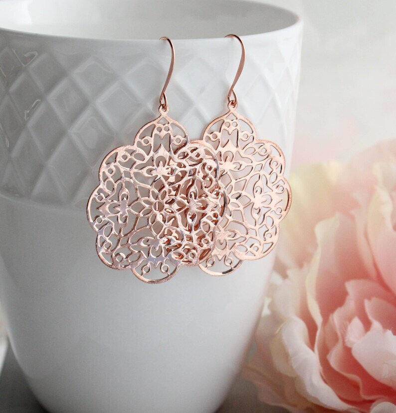 May include: Rose gold filigree earrings with a delicate floral design. The earrings are dangle style and have a hook fastening.