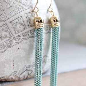 May include: A pair of gold tone earrings with long, light blue tassel drops.
