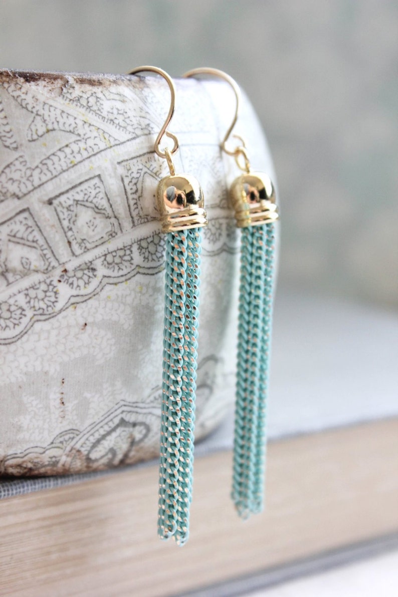 May include: A pair of gold tone earrings with long, light blue tassel drops.