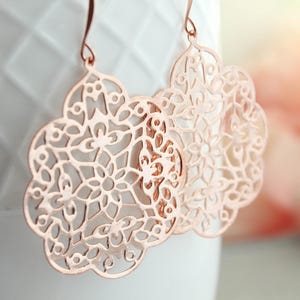 May include: Rose gold filigree earrings with a delicate, intricate design. The earrings are lightweight and dangle from a hook.
