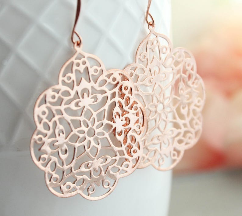 May include: Rose gold filigree earrings with a delicate, intricate design. The earrings are lightweight and dangle from a hook.