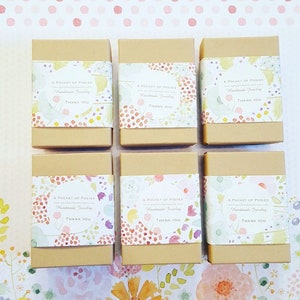May include: Six small, brown cardboard boxes with floral patterned labels. Each label reads "A Pocket of Posies" and includes the text "Handmade Jewelry" and "Thank You".