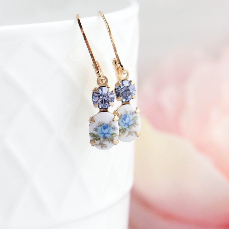 Puede incluir: Pendientes de aro dorados con un dise&ntilde;o floral azul y un acento de cristal azul claro.
