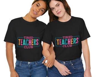 Könnte beinhalten: Zwei Frauen tragen schwarze T-Shirts mit dem Text "TIRED TEACHERS CLUB" in einem farbenfrohen Design. Der Text befindet sich in einem rechteckigen Feld mit türkisfarbenem Umriss. Die Frauen tragen blaue Jeans.
