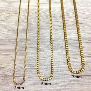 May include: Three gold-coloured chain necklaces of varying thicknesses: 3mm, 5mm, and 7mm. Each chain is displayed against a light wood-grain background. The chains are all the same colour and style, with a curb link design.