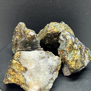 May include: Four rough pyrite specimens with a metallic gold sheen and patches of white quartz. The mineral pieces are displayed against a dark background, showcasing their natural, irregular shapes and textures. The pyrite crystals have a sparkling, iridescent quality.