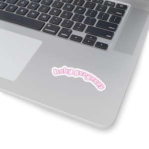 May include: A white sticker with the text "hahy gorgeous" in a pink, curved font. The sticker is placed on a silver laptop, with the keyboard visible in the background.