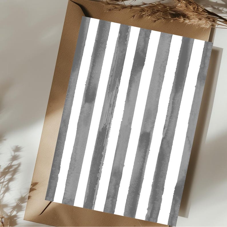 May include: A greeting card with a watercolor design of vertical gray and white stripes. The card is placed inside a brown envelope, with a sprig of dried grass in the background.