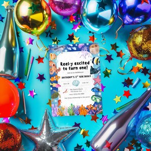 May include: A birthday party invitation with an underwater theme, featuring colorful sea creatures and the text "Reel-y excited to turn one!" on a blue background. The scene includes balloons, confetti, and star-shaped decorations.