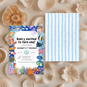 May include: A birthday invitation with an aquatic theme. The invitation features colorful illustrations of sea creatures, coral, and the text "Reel-y excited to turn one!" The back of the invitation has a blue and white striped pattern.