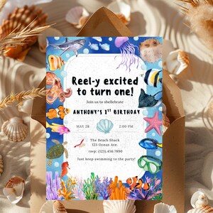 May include: A blue and white invitation with an underwater theme. The text reads "Reel-y excited to turn one!" with details for Anthony's 1st birthday. The invitation features illustrations of various sea creatures and coral.