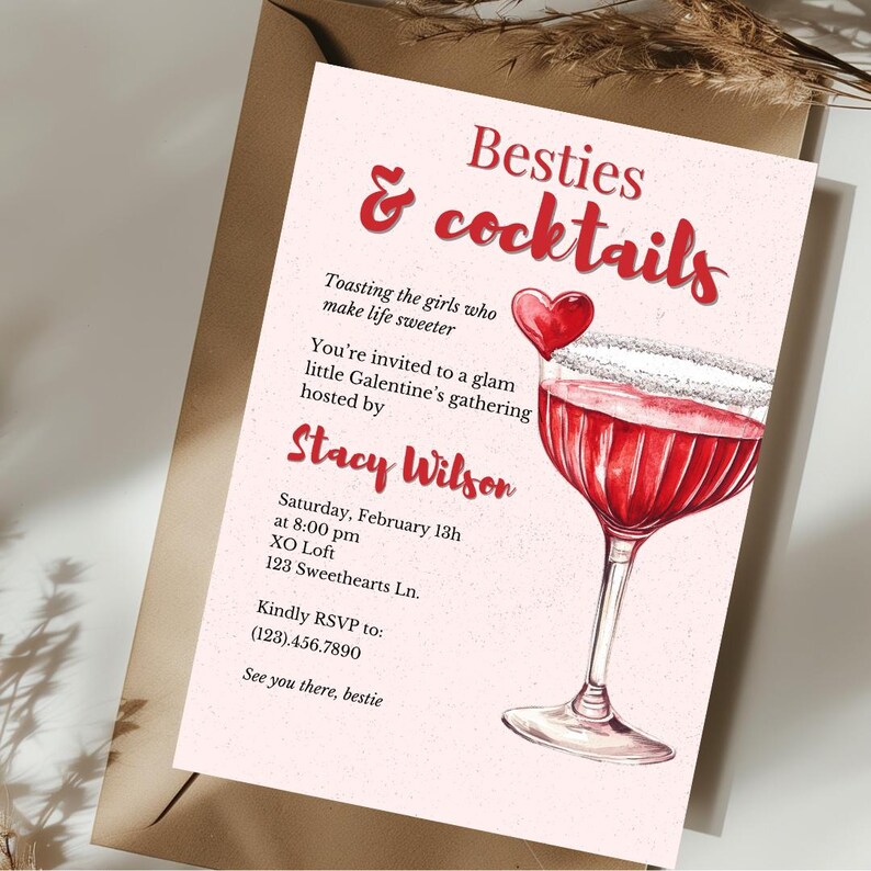 以下が含まれることがあります： 「Besties & cocktails」の赤い筆記体で書かれたピンク色のバレンタインデーの招待状。招待状には、カクテルの水彩イラストとハートが含まれています。テキストは、Stacy Wilsonが主催する集まりにゲストを招待しています。