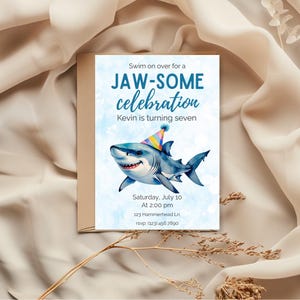 May include: A birthday party invitation with a watercolor illustration of a smiling shark wearing a party hat. The invitation reads "Swim on over for a JAW-SOME celebration" and includes event details.