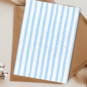 May include: A greeting card with a light blue and white striped pattern, resting on a brown envelope. The card's design features vertical stripes with a textured, distressed appearance. The envelope is a simple, neutral color.