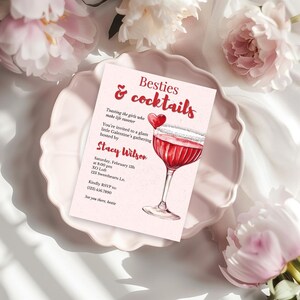 以下が含まれることがあります： 「Besties & cocktails」の文字とカクテルグラスの水彩イラストが描かれたピンク色の招待状。 Stacy Wilsonが主催するGalentine'sの集まりへの招待状です。 ピンク色のプレートの上に、ピンク色の花が添えられています。