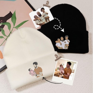 May include: Two beanies, one black and one cream-colored, each embroidered with a family portrait. The black beanie features a family of three, while the cream beanie shows a father holding a baby. The beanies are displayed with attached photos.