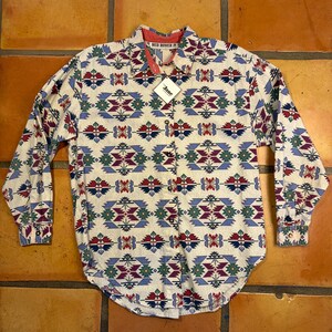 May include: A long-sleeved button-down shirt with a geometric pattern in red, blue, green, and purple on a cream background. The shirt has a red collar lining and a tag that says "Jane". The shirt is made of a lightweight fabric.