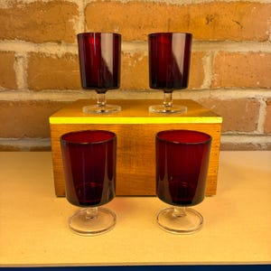 May include: A white ceramic mug with a black handle and the text "But First, Coffee" in a black, bold font. The mug is sitting on a white surface. The mug is approximately 4 inches tall.