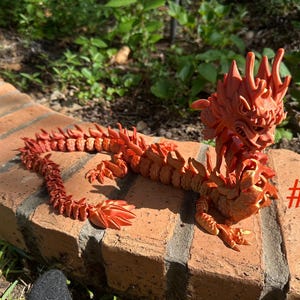 May include: A detailed, orange-red dragon figurine with intricate scales and features. The dragon is posed on a brick surface, with the number "#4" visible. The figurine is a decorative item.