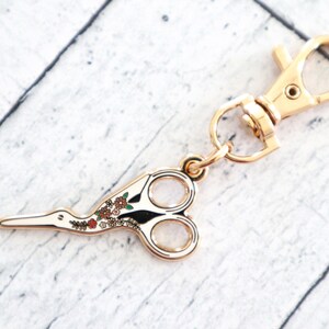May include: Gold-toned metal scissor keychain with a floral design and a lobster clasp.