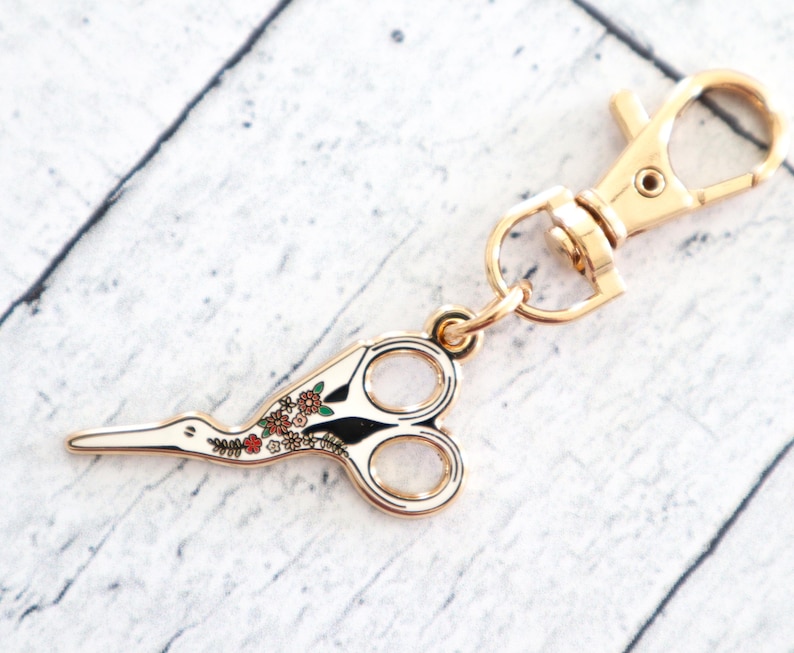 May include: Gold-toned metal scissor keychain with a floral design and a lobster clasp.