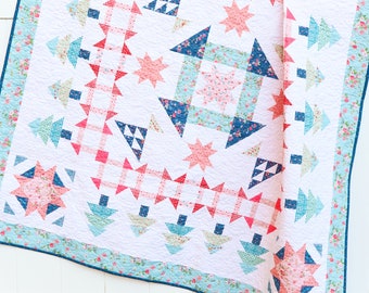 Puede incluir: Una colcha blanca con un diseño de patchwork con motivos florales rosas, azules y verdes. La colcha está colgada en una valla blanca.