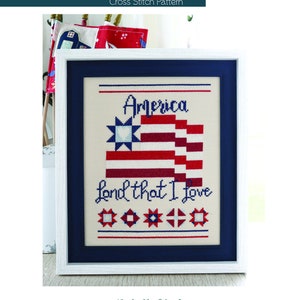 Può includere: Schema a punto croce in una cornice bianca con bordo blu navy. Il design presenta il testo "America Land That I Love" e una bandiera americana stilizzata in rosso, bianco e blu. Il motivo include stelle e forme geometriche.
